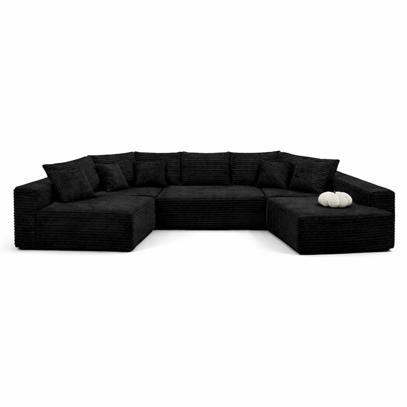 K&ouml;nnte beinhalten: Ein gro&szlig;es, schwarzes Ecksofa in U-Form mit mehreren Kissen. Das Sofa hat eine Cordstruktur. Ein kleiner, wei&szlig;er Zierk&uuml;rbis liegt auf dem Ottoman. Das Sofa ist f&uuml;r ein Wohnzimmer konzipiert.