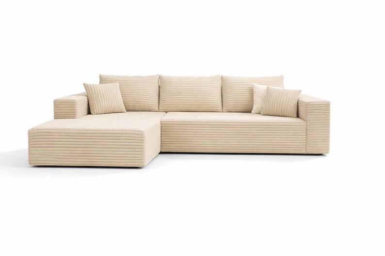 K&ouml;nnte beinhalten: Beiges Ecksofa mit Cordstruktur. Das Sofa hat eine Chaiselongue auf der linken Seite und drei quadratische R&uuml;ckenkissen. Zwei passende quadratische Kissen sind ebenfalls vorhanden. Das Sofa steht vor einem wei&szlig;en Hintergrund. Ca. 250 cm lang.