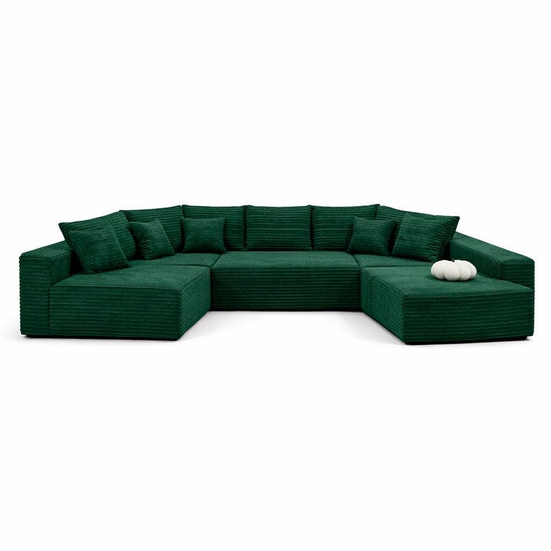 K&ouml;nnte beinhalten: Ein gro&szlig;es, U-f&ouml;rmiges Ecksofa aus gr&uuml;nem Cord mit mehreren Kissen. Das Sofa ist in einem tiefen Smaragdgr&uuml;n gehalten und hat ein modernes Design. Auf dem Ottomanen liegt ein kleiner, wei&szlig;er Zierk&uuml;rbis. Das Sofa steht vor einem wei&szlig;en Hintergrund.
