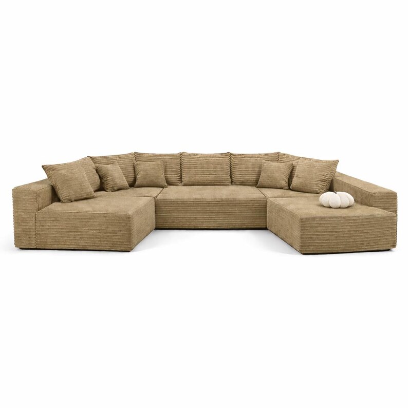 K&ouml;nnte beinhalten: Ein gro&szlig;es, modulares Ecksofa in einem neutralen Beigeton. Das Sofa hat eine Cordstruktur und enth&auml;lt mehrere quadratische Kissen und eine passende Ottomane. Ein kleines, wei&szlig;es Dekorationsobjekt liegt auf der Ottomane.