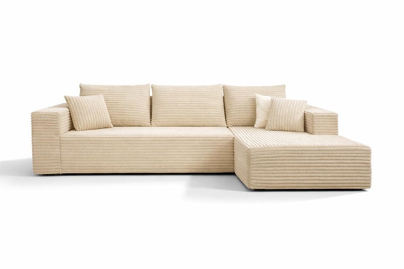K&ouml;nnte beinhalten: Beiges Ecksofa mit Cordstruktur. Das Sofa hat eine Chaiselongue auf der rechten Seite und enth&auml;lt mehrere passende quadratische und rechteckige Kissen. Die neutrale Farbe und das schlichte Design passen zu verschiedenen Einrichtungsstilen.