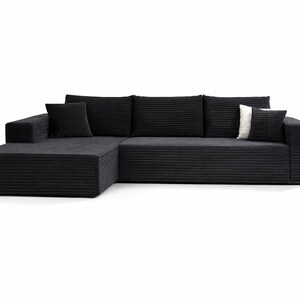 K&ouml;nnte beinhalten: Ein modernes schwarzes Ecksofa mit Cordstruktur. Das Sofa hat eine Chaiselongue auf der linken Seite und enth&auml;lt drei passende R&uuml;ckenkissen und zwei quadratische Zierkissen. Ein Kissen ist wei&szlig; mit einem schwarzen Streifen.