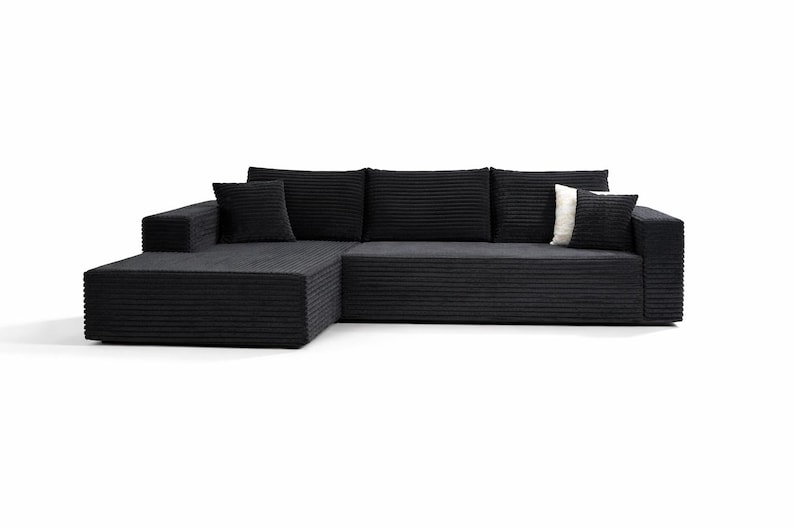 K&ouml;nnte beinhalten: Ein modernes schwarzes Ecksofa mit Cordstruktur. Das Sofa hat eine Chaiselongue auf der linken Seite und enth&auml;lt drei passende R&uuml;ckenkissen und zwei quadratische Zierkissen. Ein Kissen ist wei&szlig; mit einem schwarzen Streifen.