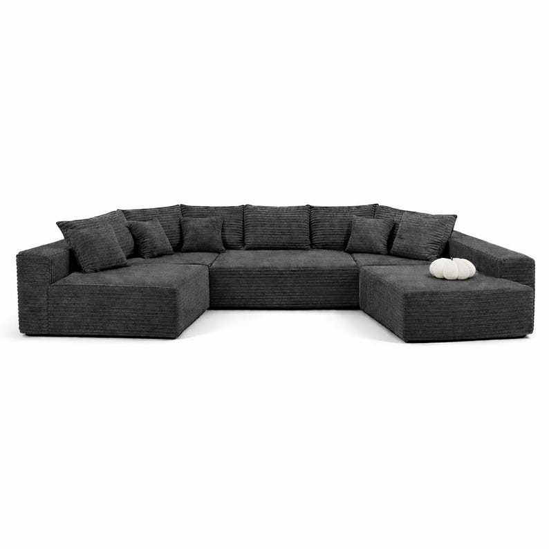 K&ouml;nnte beinhalten: Ein gro&szlig;es, dunkelgraues Ecksofa mit Cordstruktur. Das Sofa hat eine U-Form mit mehreren Kissen und Zierkissen. Ein passender Hocker ist enthalten, und ein kleiner wei&szlig;er Dekorationsgegenstand liegt auf dem Hocker.