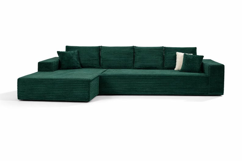 K&ouml;nnte beinhalten: Ein gro&szlig;es, smaragdgr&uuml;nes Ecksofa mit Cordstruktur. Das Sofa hat eine Chaiselongue auf der linken Seite und mehrere passende Kissen. Ein wei&szlig;es Kissen sorgt f&uuml;r Kontrast. Die M&ouml;bel stehen vor einem wei&szlig;en Hintergrund.