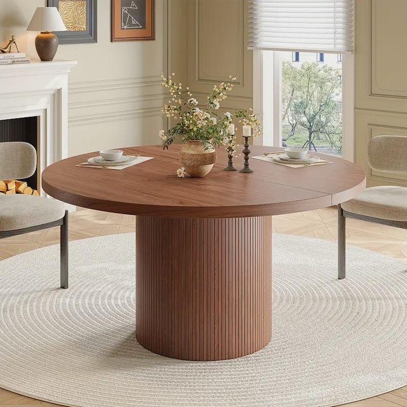 May include: A round wooden dining table with a dark brown finish. The table has a cylindrical base with vertical grooves. The table is set with plates, napkins, and a vase of flowers. The table is approximately 48 inches in diameter.