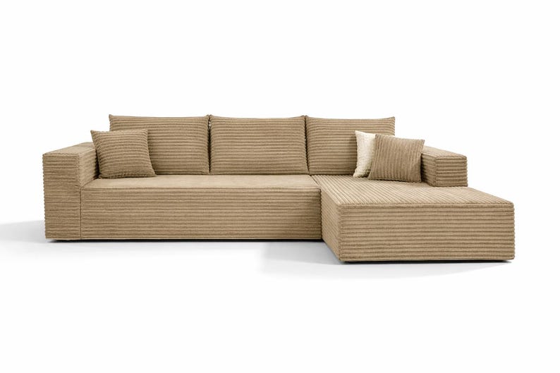 K&ouml;nnte beinhalten: Ein modernes, beiges Cord-Ecksofa mit einer Chaiselongue. Das Sofa hat ein niedriges Profil, eine breite Armlehne und mehrere passende quadratische Wurfkissen. Der Cordstoff hat eine gerippte Textur. Das Sofa steht vor einem wei&szlig;en Hintergrund.