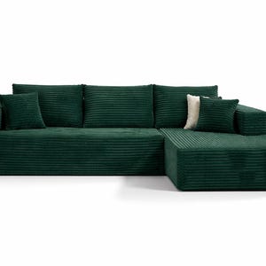 K&ouml;nnte beinhalten: Ein gro&szlig;es, smaragdgr&uuml;nes Ecksofa mit Cordstruktur. Das Sofa hat eine Chaiselongue auf der rechten Seite und enth&auml;lt mehrere passende quadratische Wurfkissen. Ein einzelnes cremefarbenes Kissen sorgt f&uuml;r Kontrast.