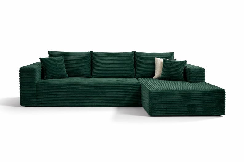 K&ouml;nnte beinhalten: Ein gro&szlig;es, smaragdgr&uuml;nes Ecksofa mit Cordstruktur. Das Sofa hat eine Chaiselongue auf der rechten Seite und enth&auml;lt mehrere passende quadratische Wurfkissen. Ein einzelnes cremefarbenes Kissen sorgt f&uuml;r Kontrast.