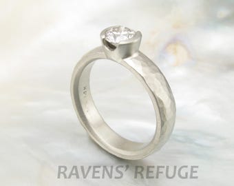 May include: A silver hammered band engagement ring with a single round diamond set in a bezel setting.