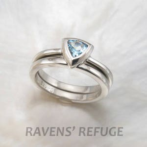 May include: A set of two silver wedding bands with a triangular aquamarine gemstone in the centre of the top band.