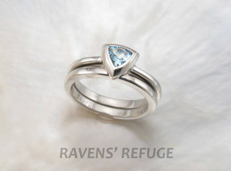 May include: A set of two silver wedding bands with a triangular aquamarine gemstone in the centre of the top band.