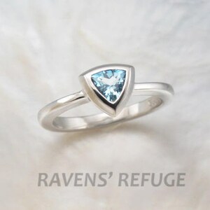 May include: A silver ring featuring a triangular blue topaz gemstone set in a bezel setting.
