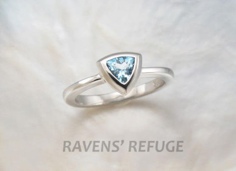 May include: A silver ring featuring a triangular blue topaz gemstone set in a bezel setting.