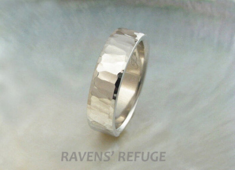 May include: A silver hammered wedding band with a smooth, polished interior. The band is thick and has a slightly rounded profile.