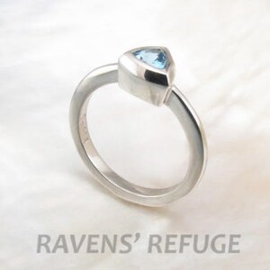 May include: A silver ring with a triangular blue gemstone set in a bezel setting.