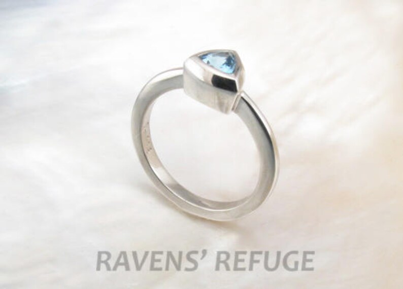 May include: A silver ring with a triangular blue gemstone set in a bezel setting.