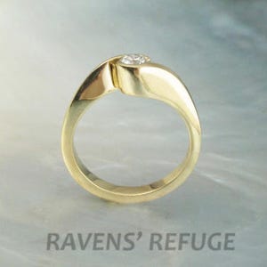 Op de afbeelding: Een gouden ring met een enkele ronde diamant in het midden. De band is gedraaid en heeft een gladde, gepolijste afwerking.