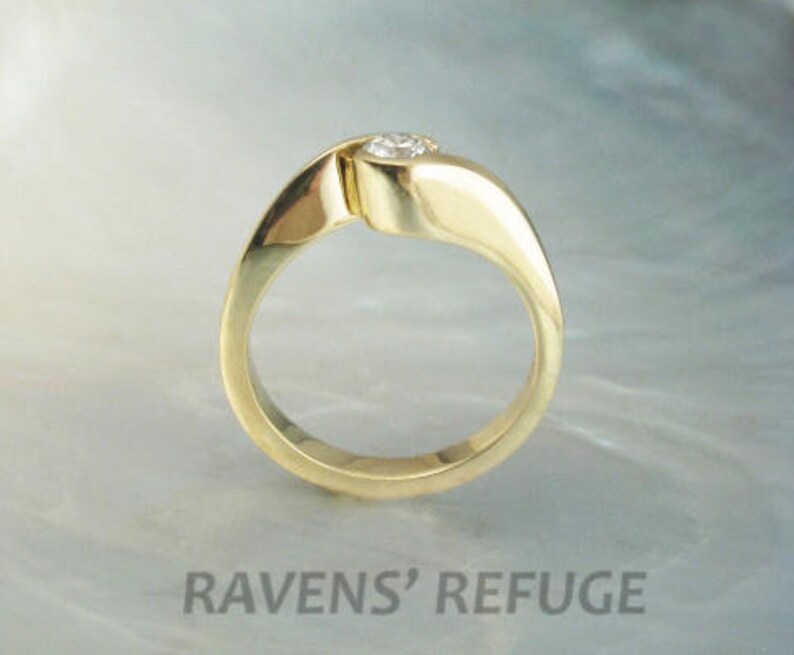 Op de afbeelding: Een gouden ring met een enkele ronde diamant in het midden. De band is gedraaid en heeft een gladde, gepolijste afwerking.