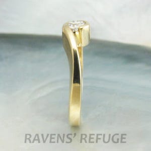 Op de afbeelding: Een gouden ring met een enkele diamant in een gebogen kraalbezetting. De band is glad en gepolijst.