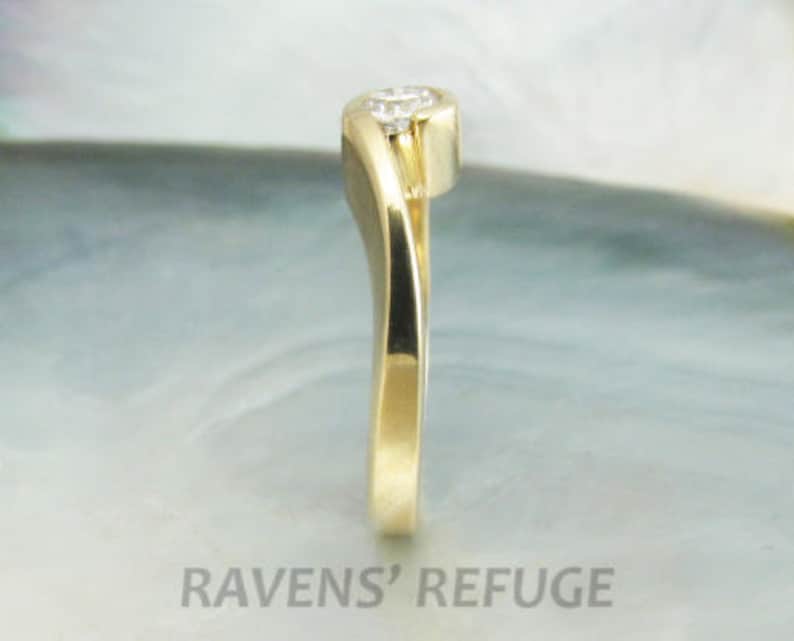 Op de afbeelding: Een gouden ring met een enkele diamant in een gebogen kraalbezetting. De band is glad en gepolijst.