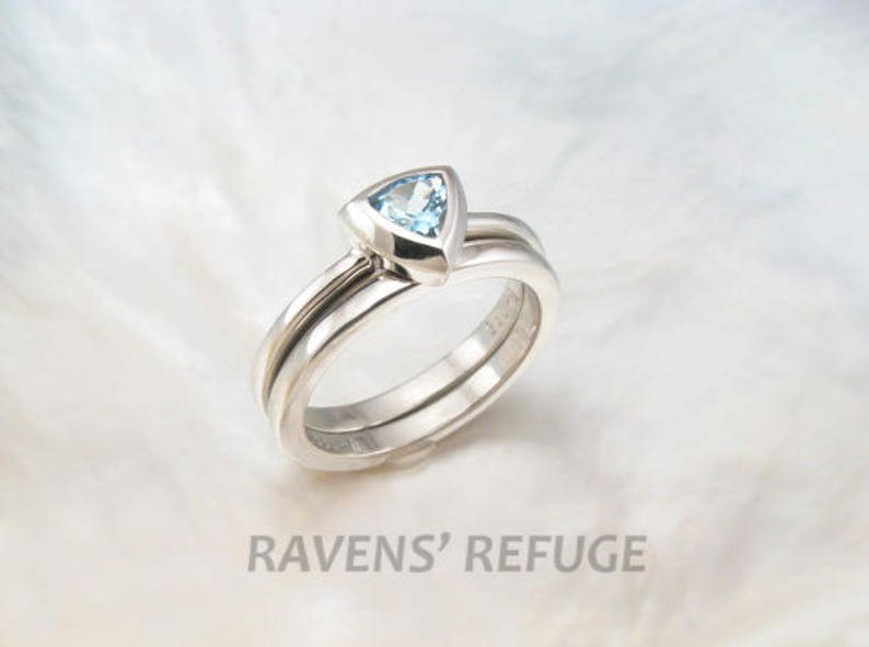 May include: A silver ring set with a triangular blue topaz gemstone. The ring is made of three bands that are twisted together.