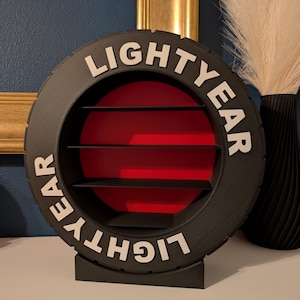 May include: A black, circular shelf unit with the word "LIGHTYEAR" in white lettering. The interior has a red background with three black shelves. The unit is designed to resemble a tire.