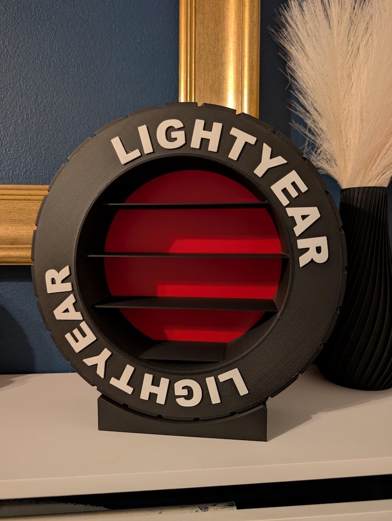 May include: A black, circular shelf unit with the word "LIGHTYEAR" in white lettering. The interior has a red background with three black shelves. The unit is designed to resemble a tire.