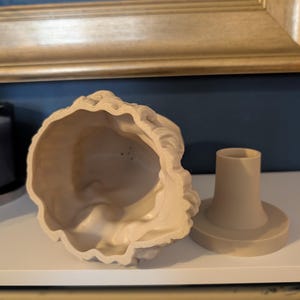 May include: A beige, decorative bust with a matching base. The bust is hollow and has a detailed, textured surface. The base is cylindrical with a circular platform. The items are displayed on a white surface.