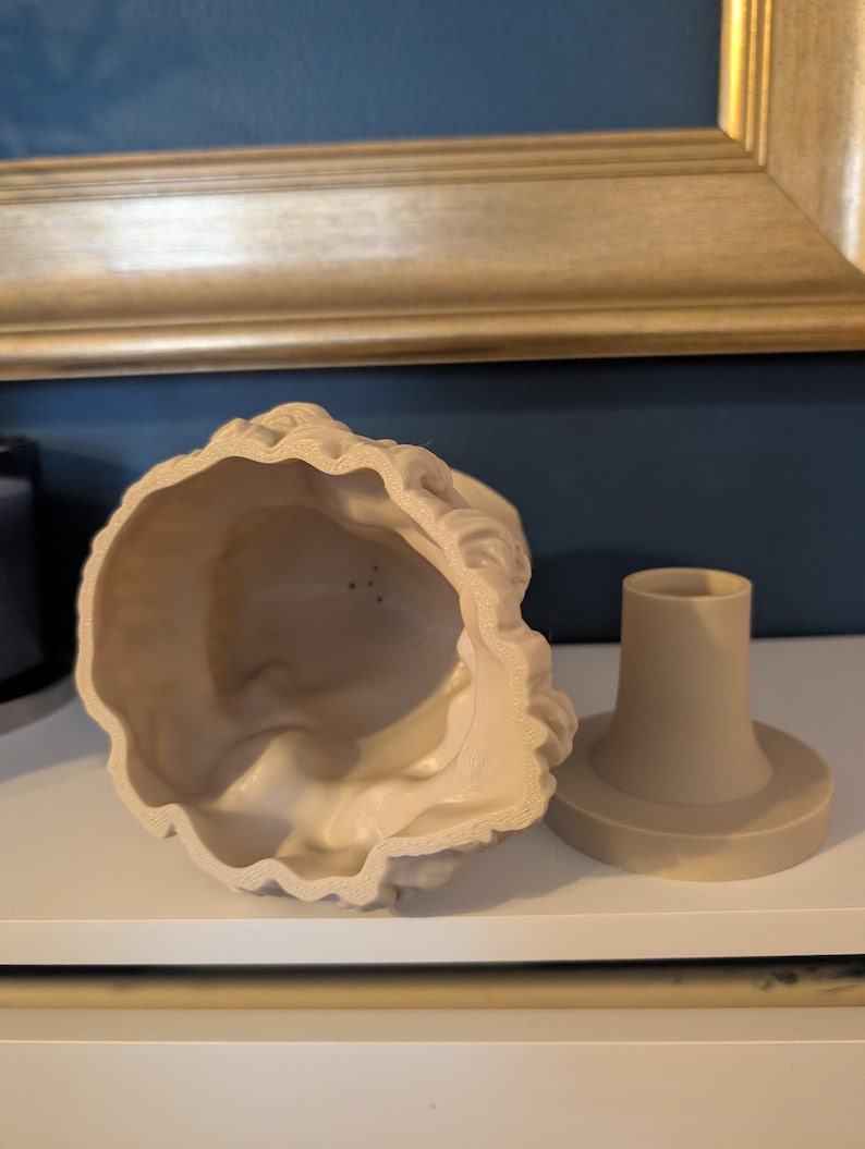 May include: A beige, decorative bust with a matching base. The bust is hollow and has a detailed, textured surface. The base is cylindrical with a circular platform. The items are displayed on a white surface.