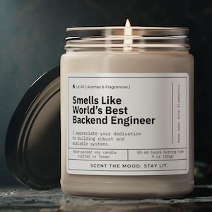 Könnte beinhalten: Eine beige Sojawachskerze in einem Glasgefäß mit schwarzem Deckel. Das Etikett lautet "Smells Like World's Best Backend Engineer". Das Etikett sagt auch "Ich schätze Ihre Hingabe beim Aufbau robuster und skalierbarer Systeme." und "50-60 Stunden Brenndauer 9 oz (250 g)". Das Etikett sagt auch "Scent the mood, stay lit."