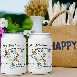 May include: Two white can coolers with a cartoon goose design, martini glass, and text. The coolers are labeled "Mrs. Silly Goose" and "Alison's Bachelorette" with "Austin Texas" below. A burlap tote bag with "HAPPY" printed on it is in the background.