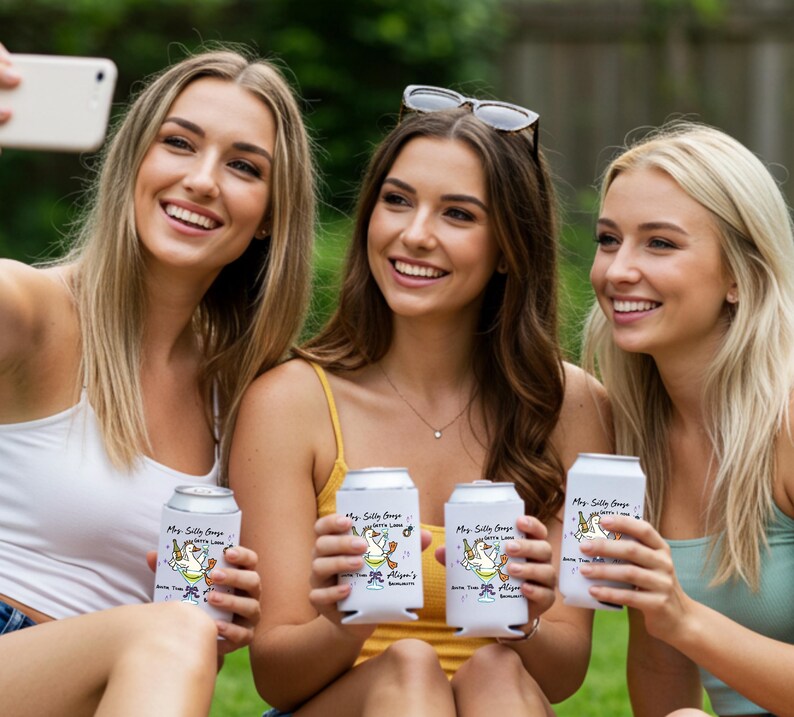 May include: Three women holding white can coolers with a cartoon goose design and text. The coolers read "My Silly Goose, Betty Lane, Join The Fun, Alison's Birthday". The women are smiling and taking a selfie.