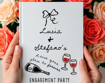 May include: A white engagement party guest book with black script that reads "Lucia + Stefano's" and "Raise your glass to forever." The book features a bow, champagne bottle, and two wine glasses. Roses in shades of peach and red are in the background.