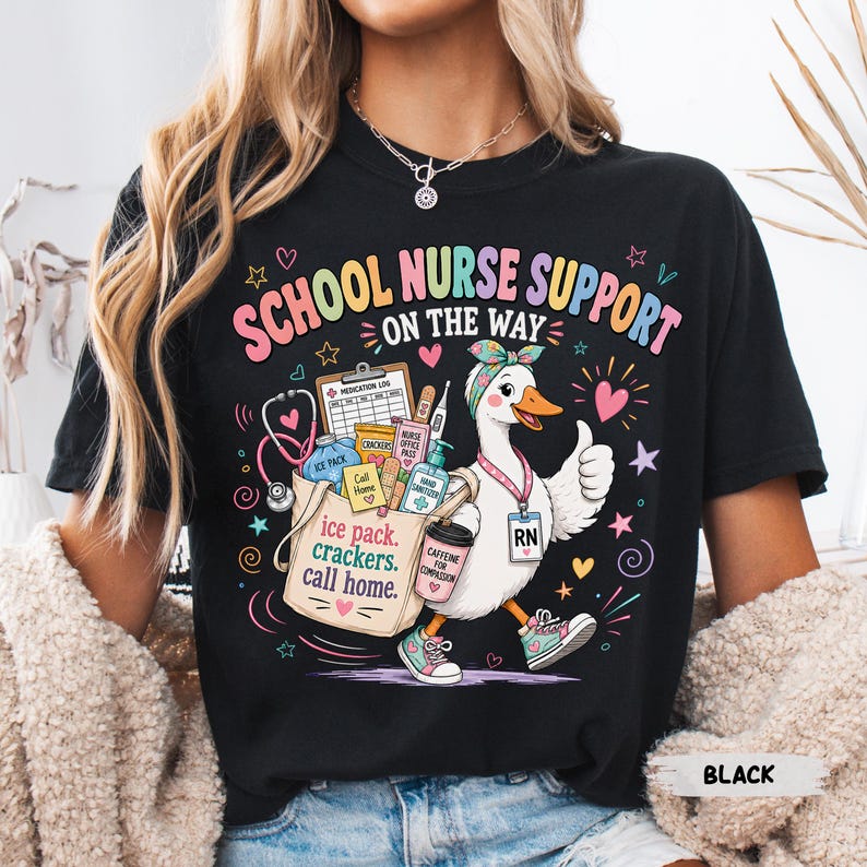 May include: A black t-shirt featuring a graphic of a white duck wearing a headband and sneakers, carrying a bag filled with medical supplies. The text reads SCHOOL NURSE SUPPORT ON THE WAY, ice pack, crackers, call home, and CAFFEINE FOR COMPASSION.