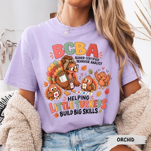 May include: A light purple t-shirt featuring a graphic of a turkey wearing glasses and a leopard print headband, holding a clipboard. The text reads BCBA BOARD CERTIFIED BEHAVIOR ANALYST HELPING LITTLE TURKEYS BUILD BIG SKILLS with colourful autumn leaves.
