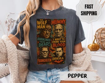 May include: Dark gray t-shirt featuring a vintage-style graphic with the Wolf Man, Mummy, Frankenstein, and Dracula. Text includes "Awakened From Dead" and "I Want to Drink Your Blood". The shirt is a classic crew neck.