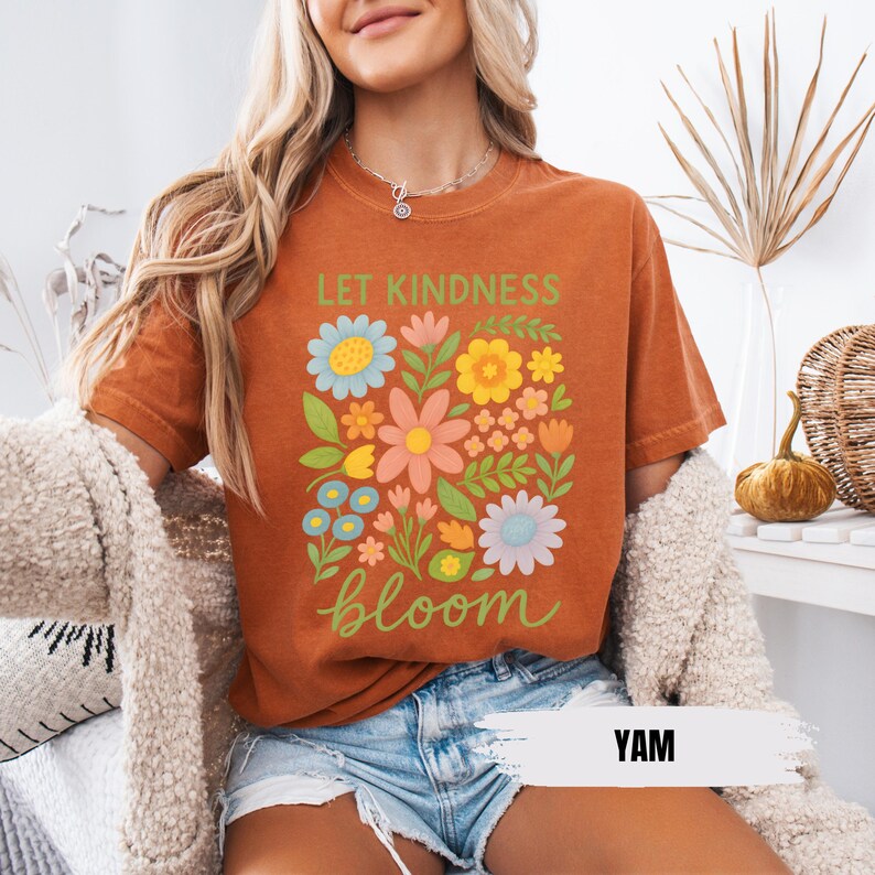Puede incluir: Una camiseta de color &oacute;xido con un dise&ntilde;o floral y el texto "Let Kindness Bloom".
