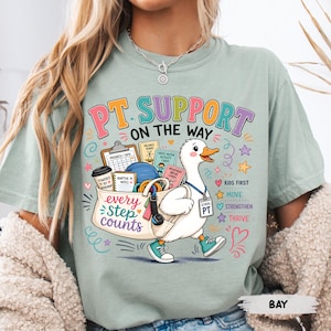Könnte beinhalten: Ein salbeigrünes T-Shirt mit einer Grafik einer weißen Ente, die eine Tasche mit Physiotherapie-Ausrüstung trägt. Der Text lautet PT SUPPORT ON THE WAY, every step counts, KIDS FIRST, MOVE, STRENGTHEN, THRIVE und SCHOOL PT.