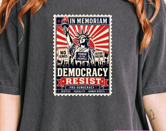 Puede incluir: Una camiseta gris carbón con un diseño gráfico estilo sello postal. El estampado muestra la Estatua de la Libertad con el texto IN MEMORIAM, DEMOCRACY, RESIST, NO KINGS, POWER TO THE PEOPLE, DEFEND FREEDOM, PRO-DEMOCRACY, JUSTICE, EQUALITY, HUMAN RIGHTS.