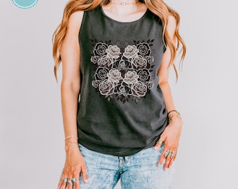 Puede incluir: Una camiseta sin mangas de color gris carbón con un estampado gráfico central de varias rosas en tonos blancos, grises y negros. La prenda tiene un cuello redondo y se combina con unos vaqueros de mezclilla azul claro con efecto lavado.