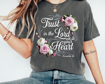 Peut inclure: T-shirt gris foncé avec l'inscription "Trust in the Lord with all your Heart" et un motif floral rose et blanc. Le texte "Proverbes 3:5" est en dessous. Le t-shirt est de style décontracté.