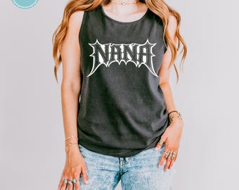 Puede incluir: Una camiseta sin mangas de color gris carbón con la palabra NANA impresa en blanco en una fuente estilizada y dentada inspirada en el metal en el pecho. La prenda se combina con unos vaqueros de mezclilla azul claro con efecto lavado.