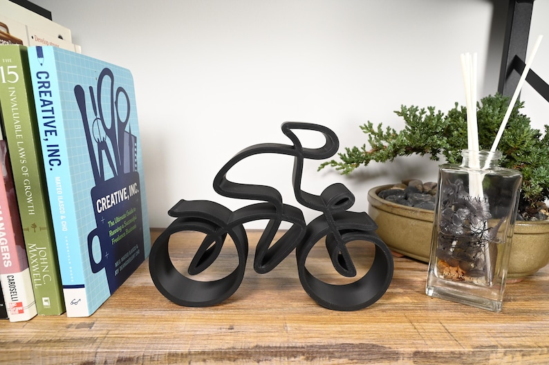 Minimalist road cyclist sculpture in a continuous line style, manufactured from plastic and displayed on a shelf or tabletop in a modern home setting—perfect for sports enthusiasts or contemporary interior décor.