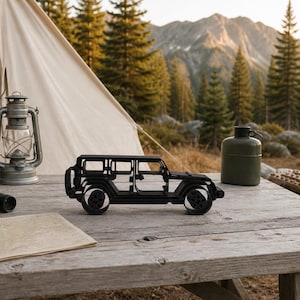 Black freestanding Jeep Wrangler 4 Door Side View line-art sculpture displayed outdoors in a alpine forest overland basecamp at a mountain trailhead.