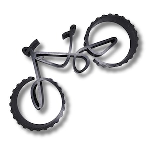 Minimalist bicycle sculpture with hollow frame and thick, ridged wheels, viewed from above at an angle. Displayed on a white surface, showing detailed layering texture and shadows beneath the object.