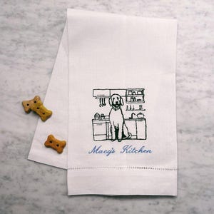 May include: White kitchen towel with black embroidery of a dog standing in a kitchen with the text "Macy's Kitchen" in blue.