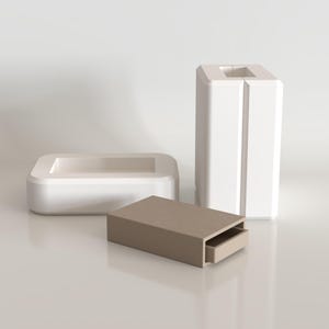 May include: A set of three objects including a white rectangular tray with rounded corners, a tall white vertical block with a central slit, and a small rectangular beige box with a sliding drawer component positioned in the foreground.