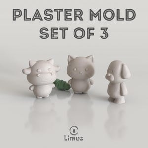Puede incluir: Un juego de tres moldes de yeso con forma de vaca, gato y perro. La vaca tiene cuernos, el gato orejas puntiagudas y el perro orejas caídas. Los moldes son de color gris claro. El texto "PLASTER MOLD SET OF 3" está en la parte superior.
