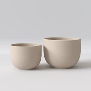 May include: Two round, beige ceramic planters with a matte, textured finish. The planters are bowl-shaped with open tops and curved bases, displayed side-by-side with one being slightly smaller than the other, set against a neutral background.